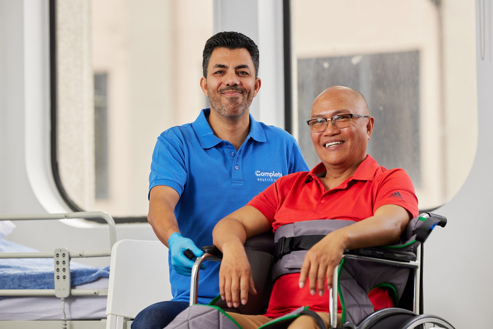 A support worker standing beside a smiling client in a wheelchair during a care training session