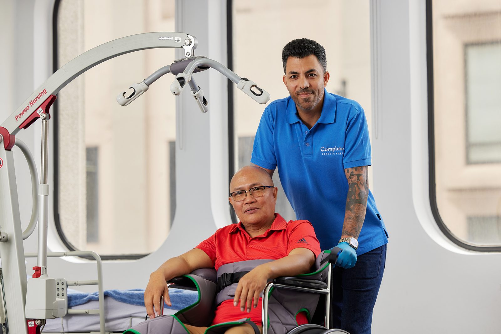 A carer assisting a seated client beside a patient hoist, demonstrating the equipment used in Australian aged care